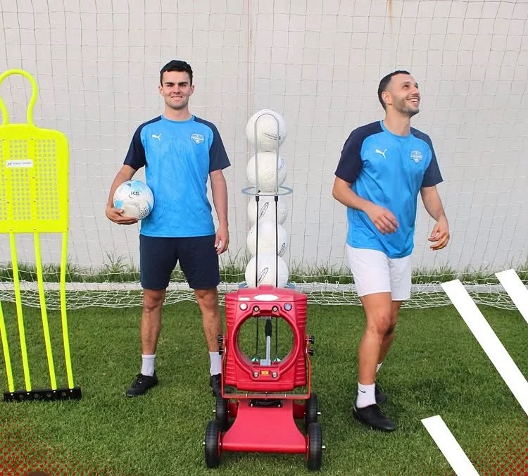 Two players with a red POWAPASS machine in front of a goal and training mannequin